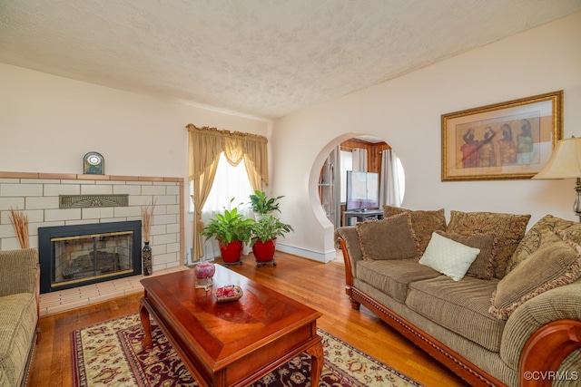 living room with a brick fireplace, arched walkways, a textured ceiling, and wood finished floors