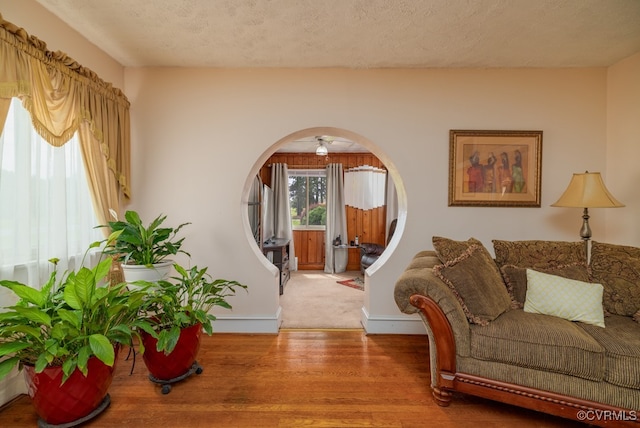 living area featuring a textured ceiling, baseboards, ceiling fan, and wood finished floors