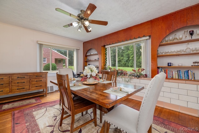 dining room with a ceiling fan, a textured ceiling, built in features, and light wood-style floors