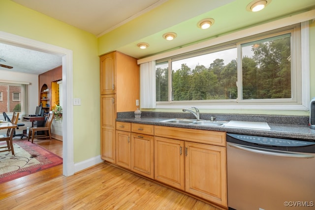 kitchen with a sink, dark countertops, stainless steel dishwasher, and light wood-style flooring