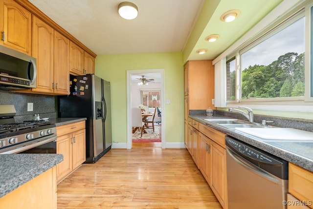 kitchen featuring appliances with stainless steel finishes, tasteful backsplash, a sink, baseboards, and light wood-style flooring