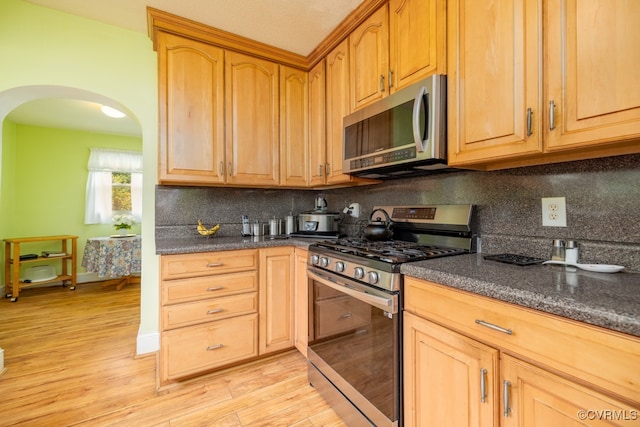 kitchen with arched walkways, backsplash, stainless steel appliances, and light wood finished floors