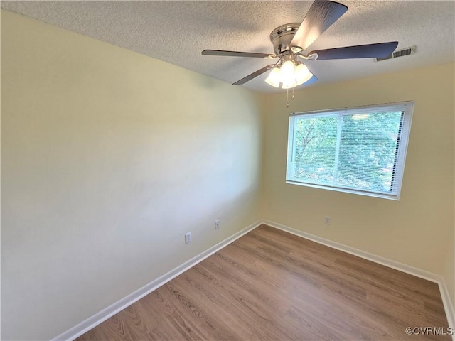 empty room with visible vents, wood finished floors, baseboards, ceiling fan, and a textured ceiling