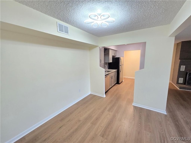 interior space with a textured ceiling, visible vents, light wood-type flooring, a sink, and baseboards