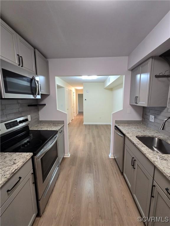 kitchen with a sink, stainless steel appliances, decorative backsplash, light wood-type flooring, and gray cabinetry