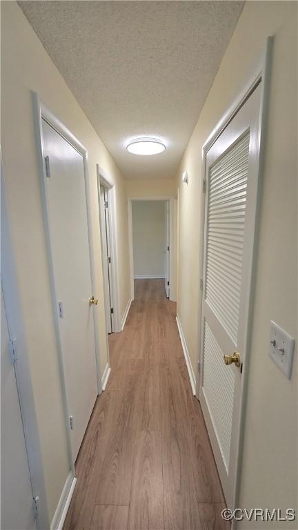 hallway featuring baseboards, a textured ceiling, and light wood-style flooring