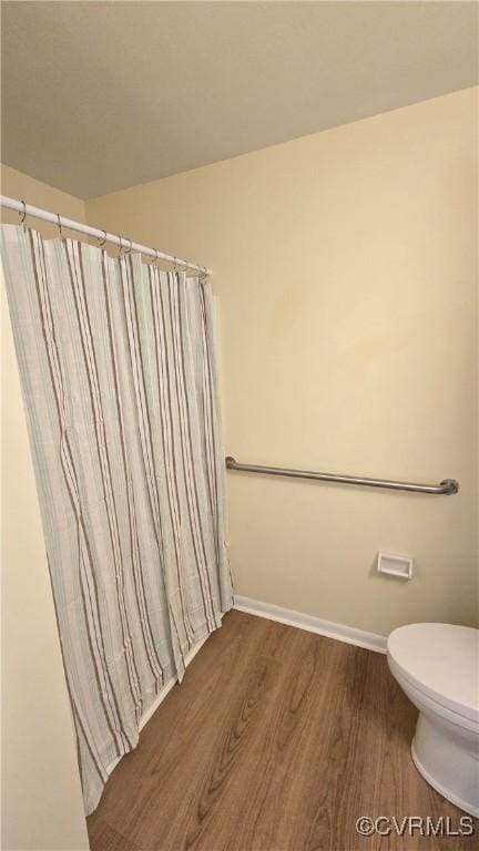 bathroom with baseboards, a shower with curtain, toilet, and wood finished floors