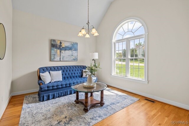 living room with baseboards, a chandelier, light wood finished floors, and lofted ceiling