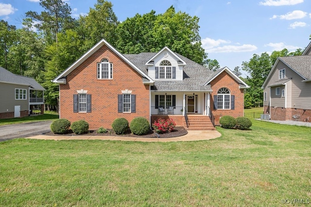 traditional-style home featuring covered porch, brick siding, a front yard, central AC unit, and roof with shingles