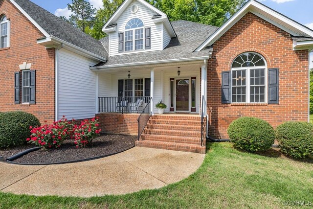 view of front facade featuring a porch, a shingled roof, brick siding, and a front lawn