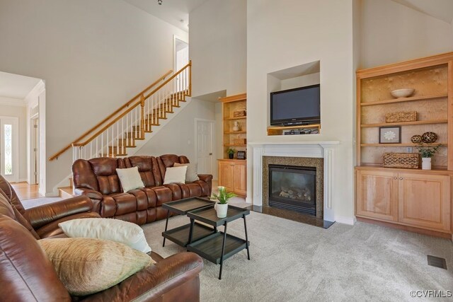 carpeted living area with high vaulted ceiling, built in shelves, stairway, a premium fireplace, and baseboards