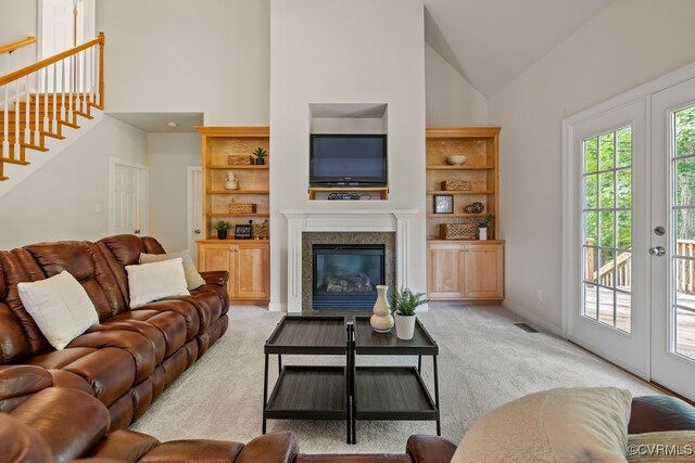 living room with light carpet, stairway, high vaulted ceiling, a fireplace, and built in shelves