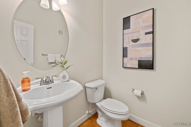 bathroom with baseboards, toilet, wood finished floors, and a sink