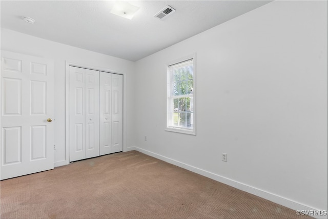 unfurnished bedroom featuring baseboards, light colored carpet, visible vents, and a closet