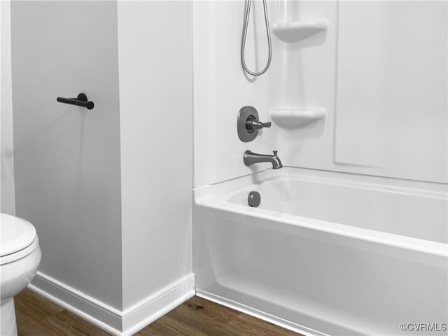 bathroom with baseboards, wood finished floors, bathtub / shower combination, and toilet
