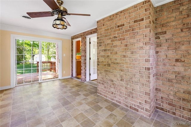 empty room featuring a ceiling fan, brick wall, visible vents, and baseboards
