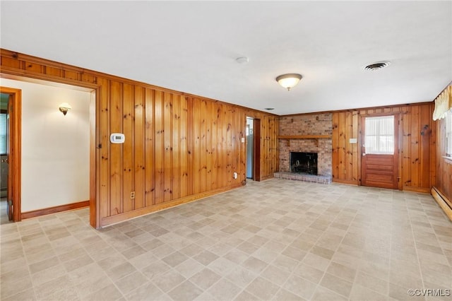 unfurnished living room with visible vents, baseboards, a brick fireplace, and wooden walls