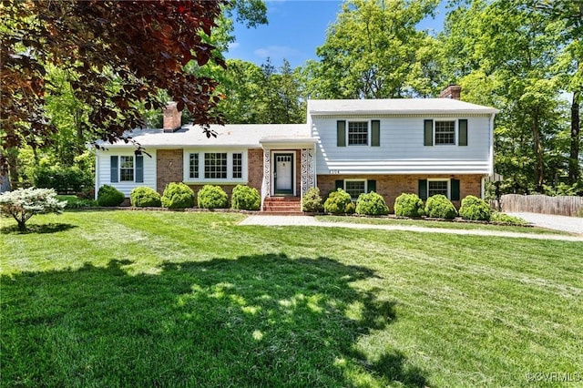 tri-level home with brick siding, fence, a chimney, and a front lawn