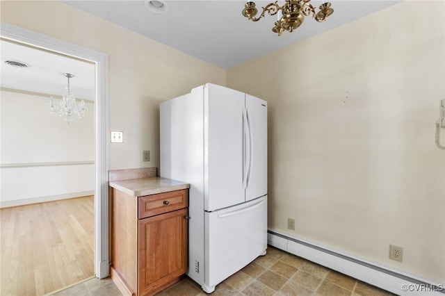 kitchen featuring brown cabinetry, visible vents, a baseboard radiator, freestanding refrigerator, and a notable chandelier