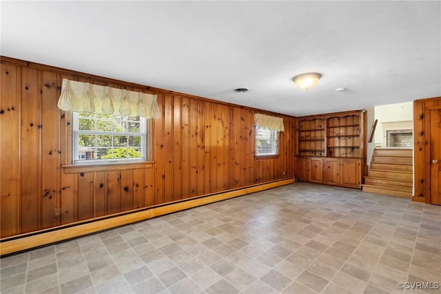 spare room featuring wood walls, light floors, stairs, and baseboard heating