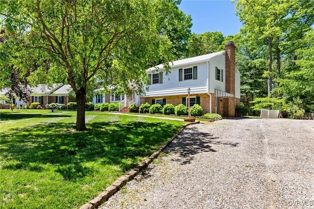 split level home with brick siding, a front yard, driveway, and a chimney