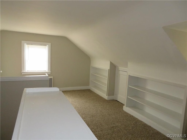 bonus room with light carpet, built in shelves, radiator, baseboards, and vaulted ceiling