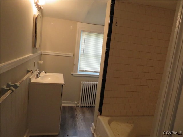 bathroom with wood finished floors, shower / bathtub combination, radiator heating unit, and vanity