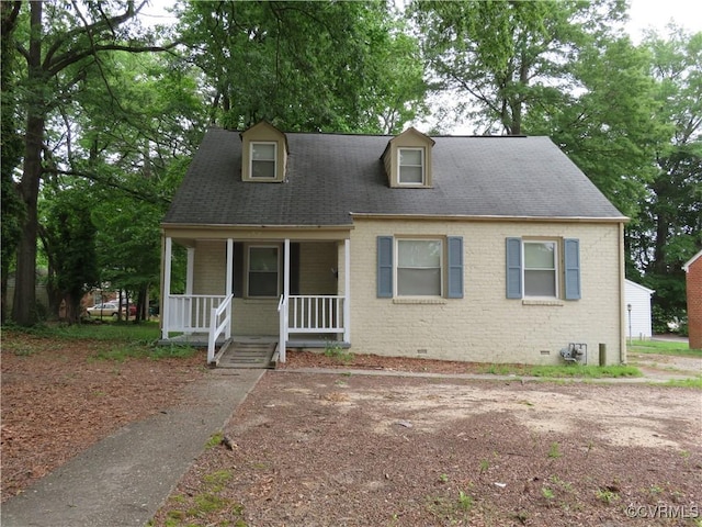 cape cod home with covered porch, crawl space, a shingled roof, and brick siding