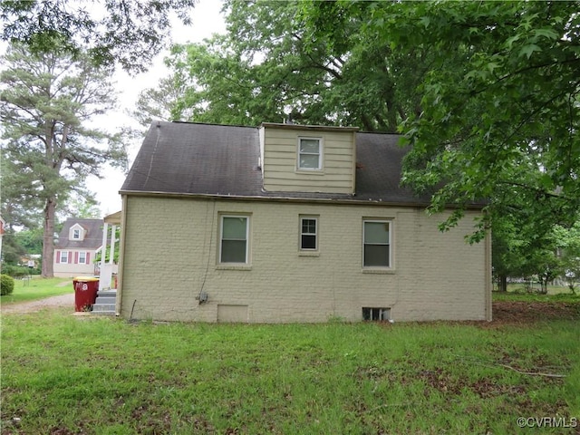 rear view of property with a lawn, a shingled roof, and brick siding