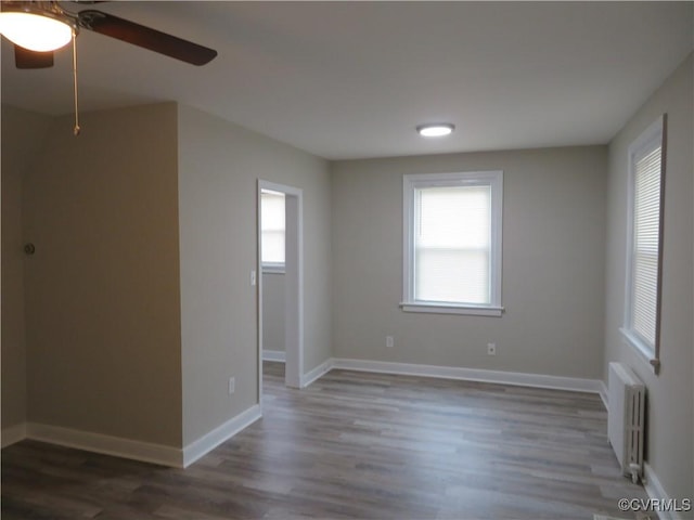 unfurnished room featuring ceiling fan, a wealth of natural light, radiator, and wood finished floors