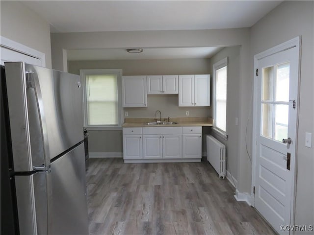 kitchen featuring freestanding refrigerator, a sink, radiator heating unit, and white cabinets