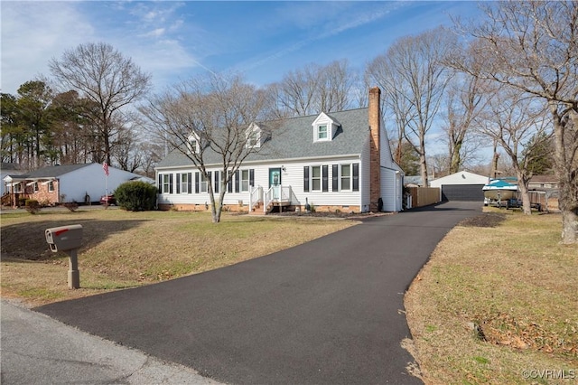 new england style home with a detached garage, a chimney, roof with shingles, and a front lawn