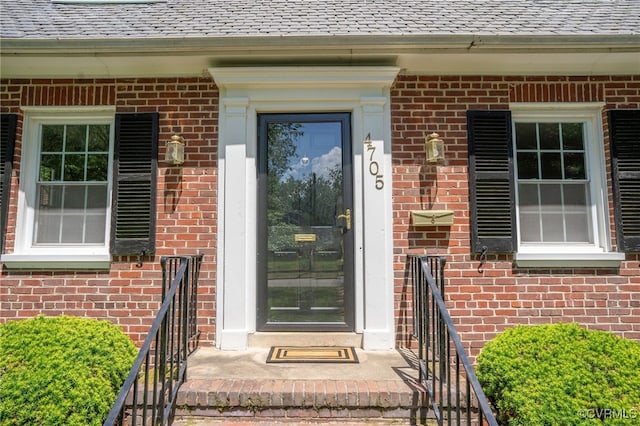 view of exterior entry with brick siding and a shingled roof