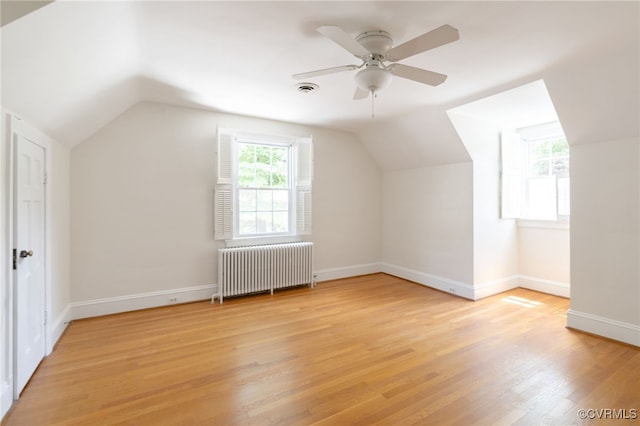 additional living space with a ceiling fan, vaulted ceiling, radiator heating unit, and light wood-style flooring