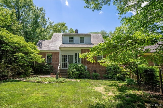 back of house with a lawn, a chimney, entry steps, and brick siding