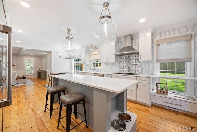 kitchen featuring tasteful backsplash, white cabinets, wall chimney exhaust hood, and visible vents