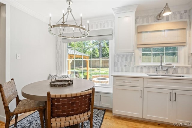 kitchen with a sink, light countertops, light wood finished floors, a chandelier, and ornamental molding