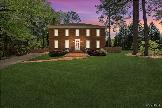 colonial inspired home featuring concrete driveway, a chimney, and a yard