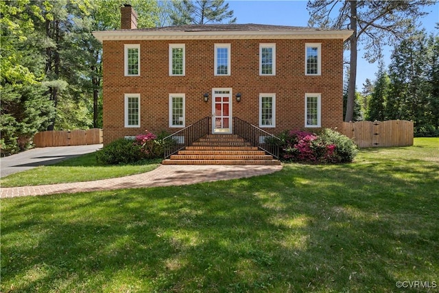 colonial inspired home featuring a chimney, a front lawn, and brick siding