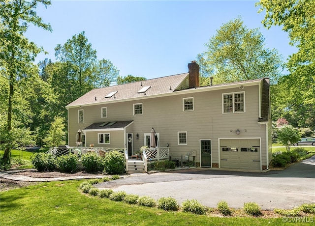 rear view of house featuring an attached garage, driveway, a wooden deck, and a chimney
