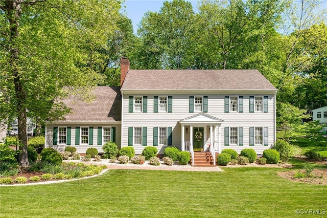 colonial home featuring a shingled roof, a chimney, and a front lawn