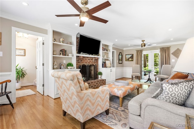 living room featuring ornamental molding, a fireplace, a ceiling fan, and light wood finished floors