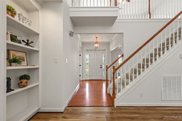 foyer entrance featuring visible vents, ornamental molding, stairs, hardwood / wood-style floors, and baseboards