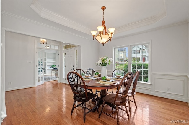dining space featuring crown molding, a raised ceiling, a notable chandelier, and light wood finished floors