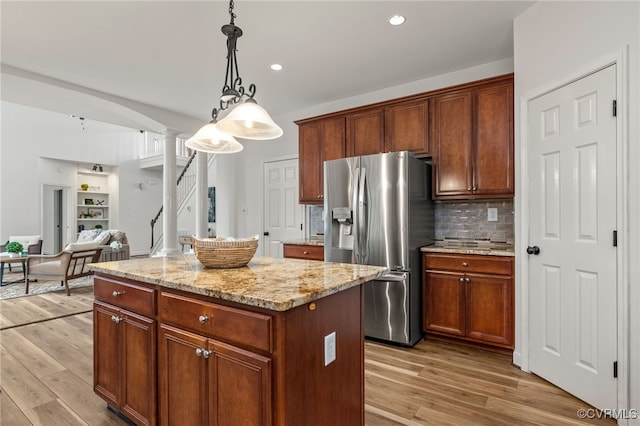 kitchen with light stone countertops, light wood finished floors, stainless steel fridge with ice dispenser, a center island, and ornate columns