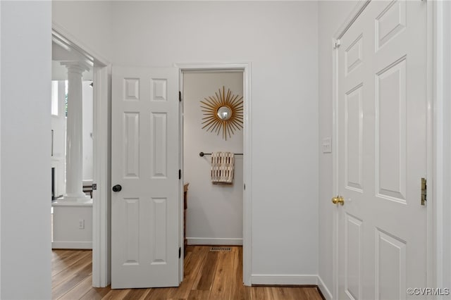 corridor featuring ornate columns, baseboards, wood finished floors, and visible vents