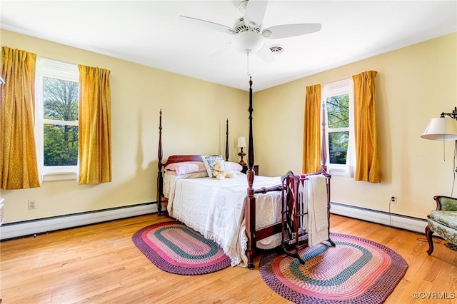 bedroom featuring a baseboard radiator, multiple windows, and wood finished floors