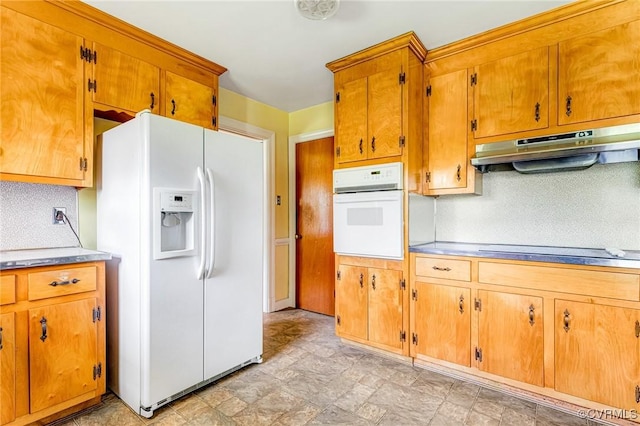 kitchen featuring brown cabinetry, stone finish flooring, tasteful backsplash, under cabinet range hood, and white appliances