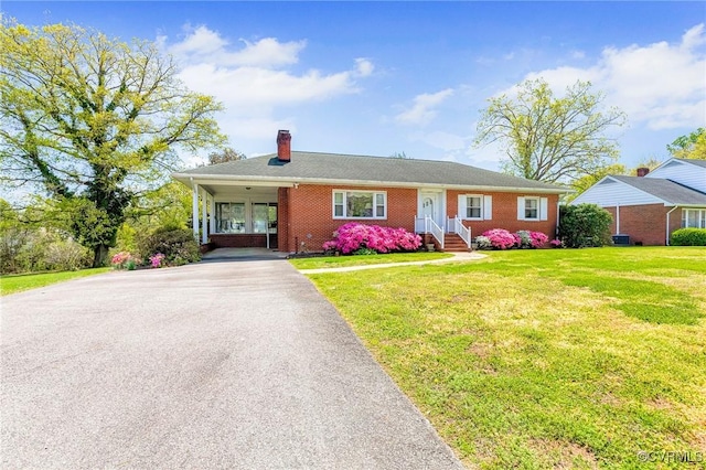 ranch-style house featuring brick siding, a chimney, a front lawn, and aphalt driveway