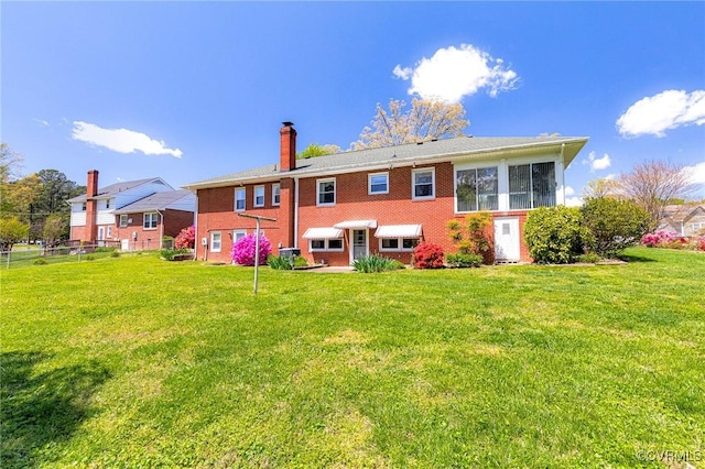 rear view of house featuring a lawn, brick siding, fence, and a chimney
